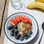 Bowl of banana zoats (zucchini oats) outside with fresh fruit on top